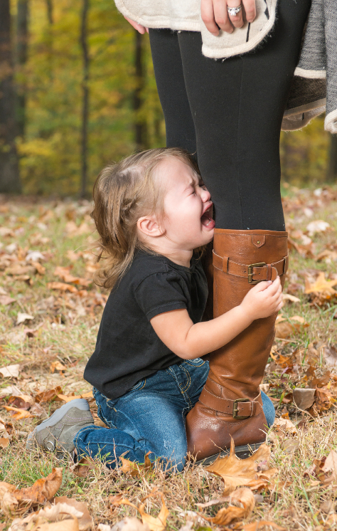 Toddler holding on to mums legs crying