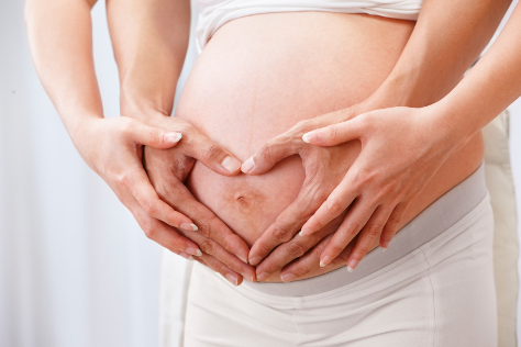 Pregnant woman with hands on bump and partners hands