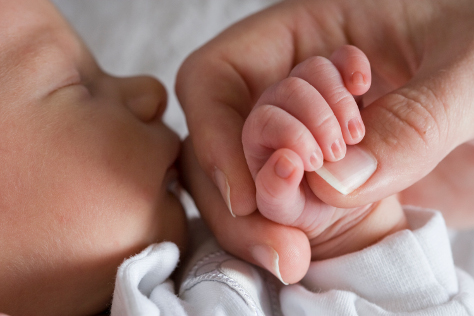 Close up baby holding mums finger