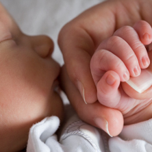 Close up baby holding mums finger